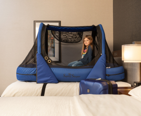 Young girl in The Safety Sleeper fully enclosed bed for home and travel. The bed is strapped to a hotel bed. The picture is taken in a hotel.