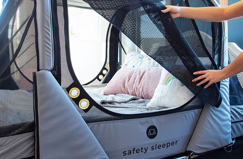 The Safety Sleeper® with its mesh door peeled back to reveal a cozy mattress inside with pillows and a blanket.